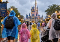 Family wearing rain ponchos walking through Walt Disney World in the rain with a stroller covered for wet weather.